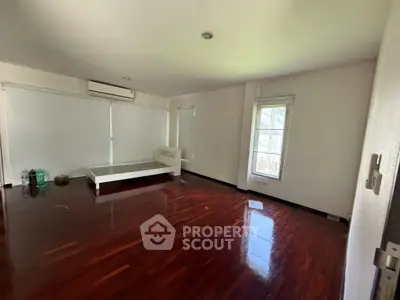 Spacious bedroom with wooden flooring and natural light, featuring a minimalist design and air conditioning.