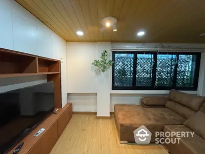 Cozy living room with modern sectional sofa and large TV, featuring wooden ceiling and floor.