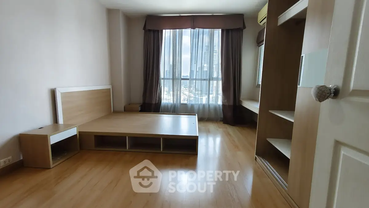 Spacious bedroom with wooden flooring and large window offering city views