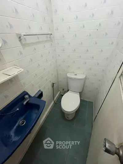 Compact bathroom with blue sink and white toilet in a tiled space.