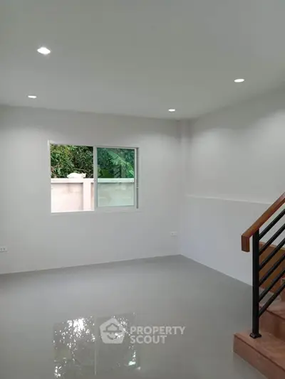 Modern minimalist living room with sleek staircase and large window overlooking greenery.