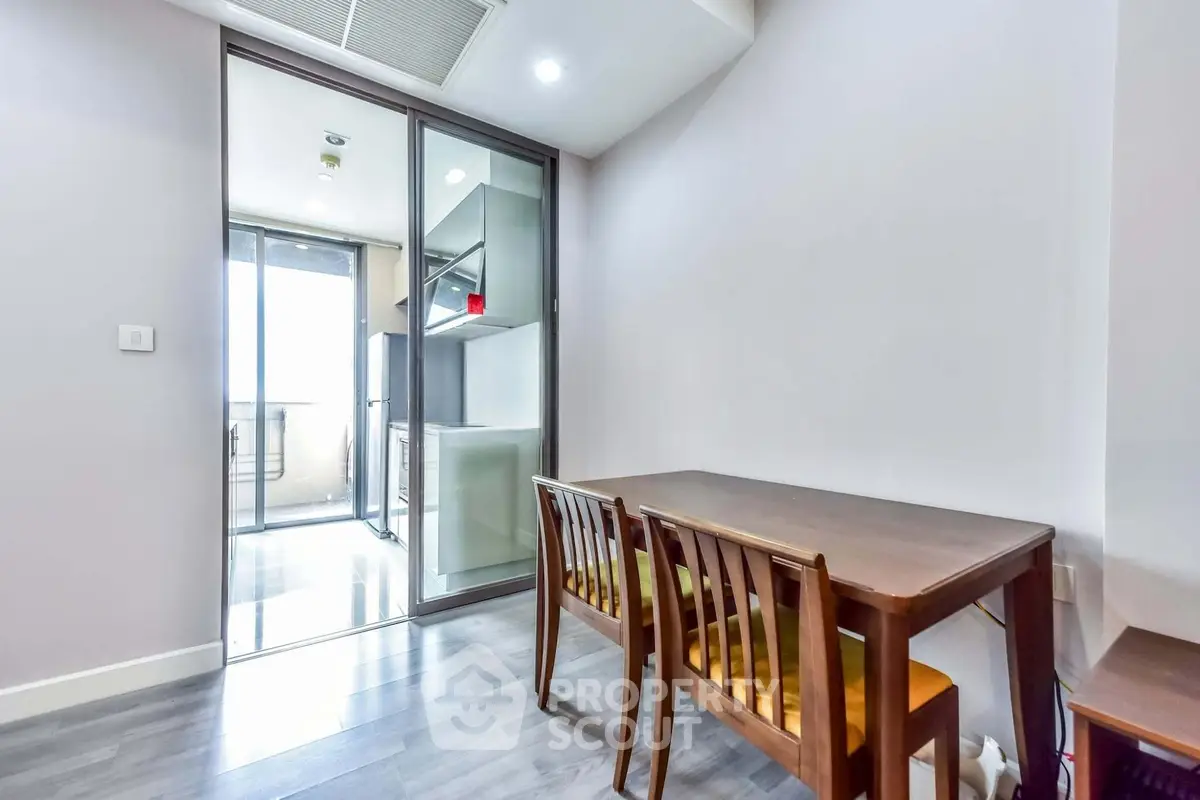 Modern dining area with wooden table and chairs, adjacent to a sleek kitchen with glass sliding doors.