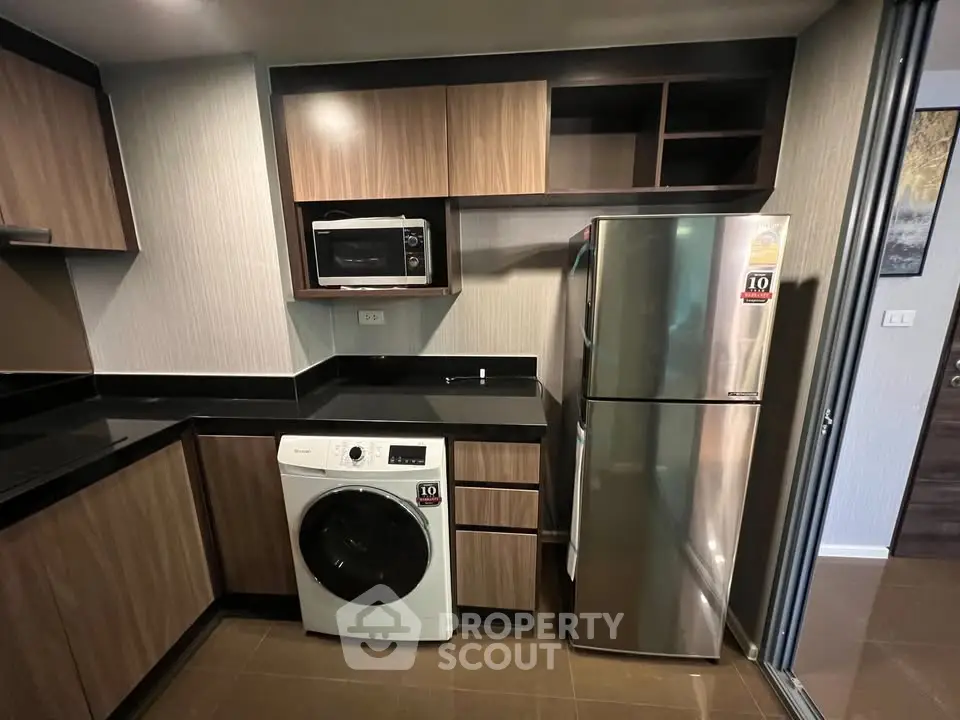 Modern kitchen with sleek appliances including washing machine and microwave, featuring elegant wood cabinetry.