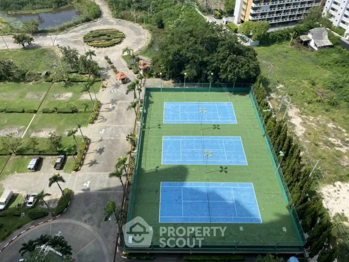 Aerial view of tennis courts in a residential complex with lush greenery and parking area.