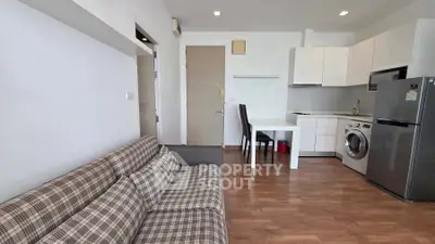 Modern open-plan living room with kitchen, featuring plaid sofa and sleek appliances.