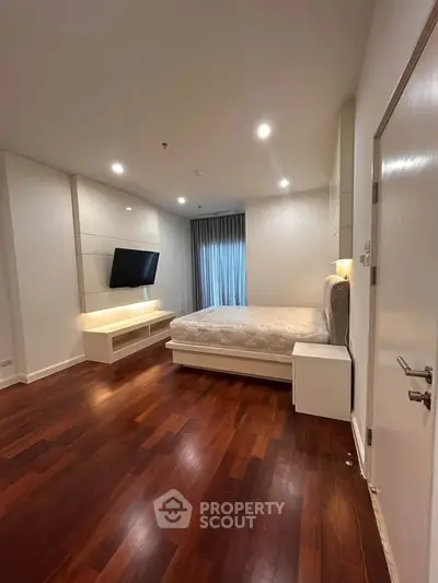 Spacious modern bedroom with wooden flooring and wall-mounted TV