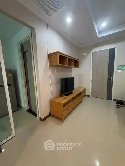 Modern living room with sleek wooden furniture and TV, adjacent to kitchen area.