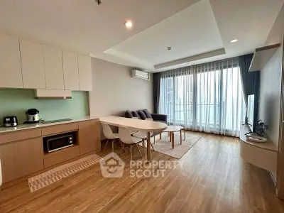 Modern living room with open kitchen, wooden flooring, and large windows for natural light.