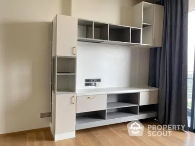 Spacious living room with modern built-in shelving unit and sleek hardwood flooring, bathed in natural light from large window.