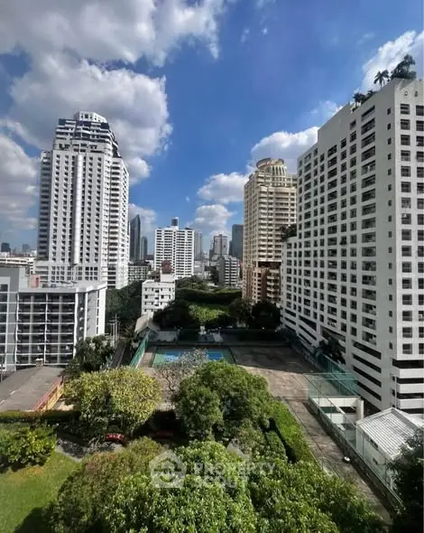 Stunning cityscape view from high-rise apartment with lush greenery and pool area.