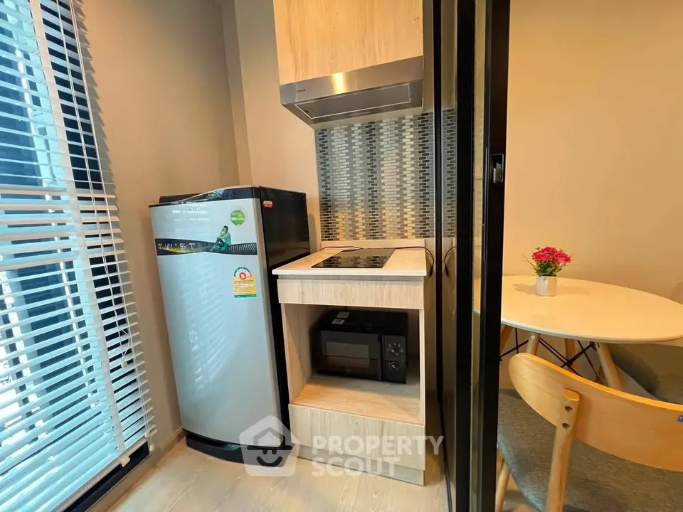 Modern compact kitchen with fridge, stove, and dining area in cozy apartment.