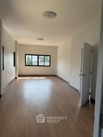 Spacious empty room with wooden flooring and large windows offering natural light.