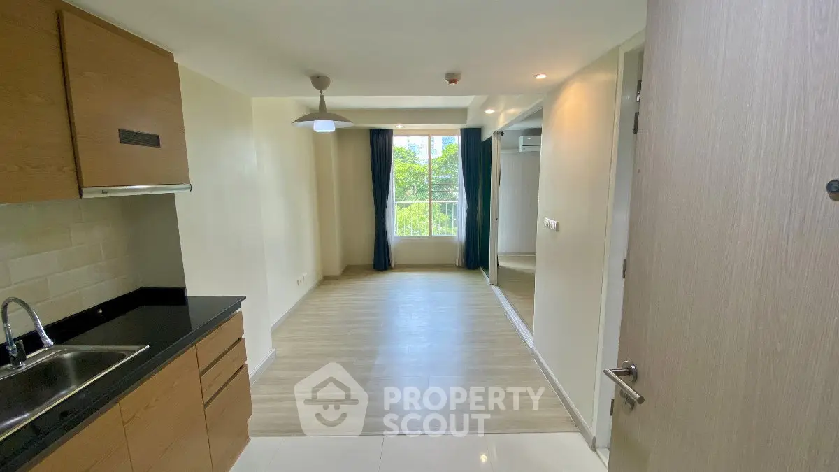Spacious apartment with modern kitchen and bright living area, featuring large window with green view.