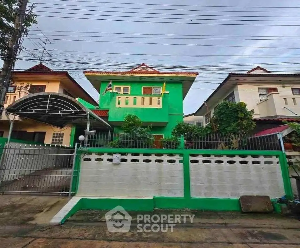 Charming two-story green house with gated entrance and lush garden in a serene neighborhood.