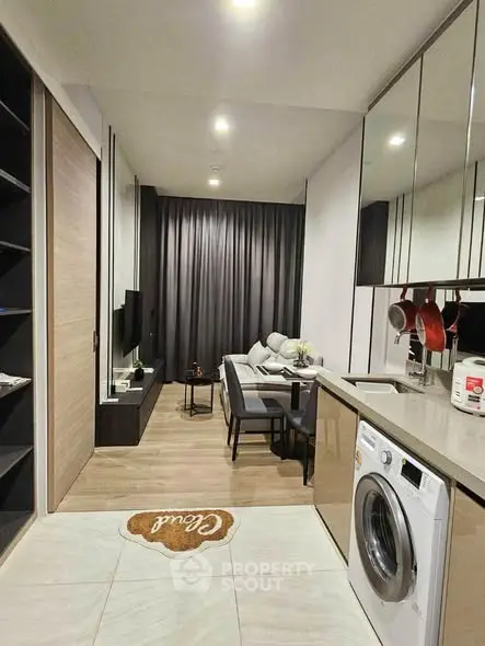 Modern living room with sleek kitchen and washing machine, featuring stylish decor and cozy ambiance.