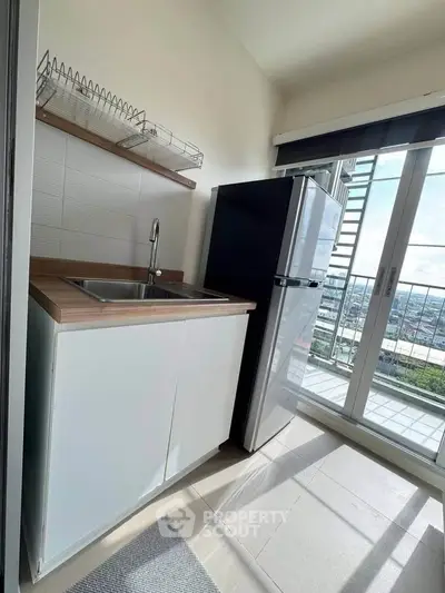 Modern kitchen with sleek design and balcony view, featuring a fridge and ample natural light.