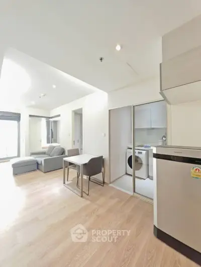 Modern open-plan living room with kitchen and laundry area in a bright apartment.