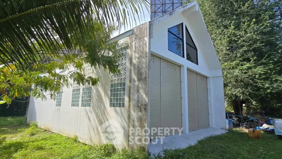 Modern warehouse with large windows and roll-up doors in lush green setting.