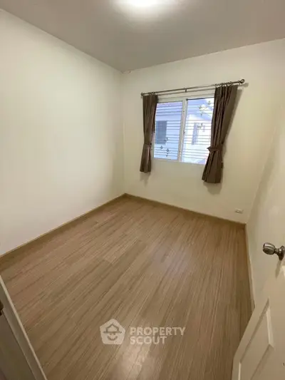 Spacious empty bedroom with wooden flooring and window view, ready for customization.