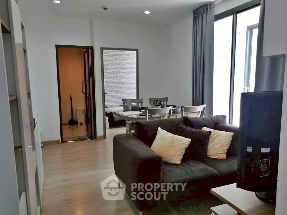 Modern living room with cozy seating and dining area, featuring large windows for natural light.