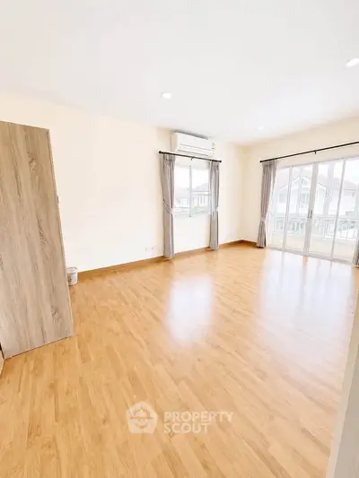Spacious empty room with wooden flooring and large windows in modern home.