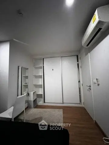 Modern bedroom with sleek white furniture and built-in wardrobe, featuring a minimalist design and air conditioning.