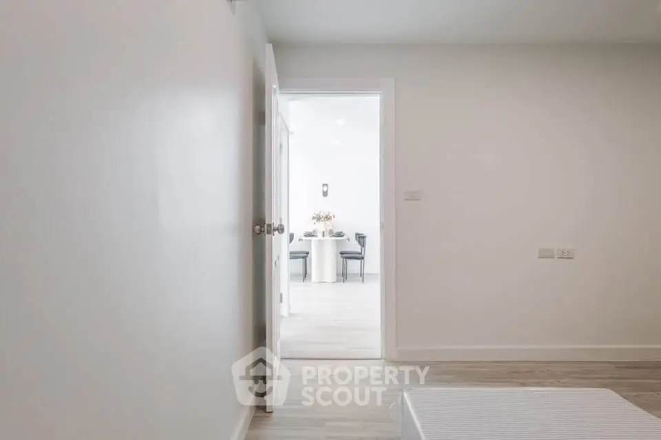 Minimalist interior with open door leading to a bright dining area, showcasing modern design and simplicity.