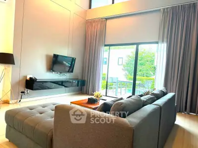 Spacious modern living room with large windows and garden view, featuring a stylish sofa and wall-mounted TV.