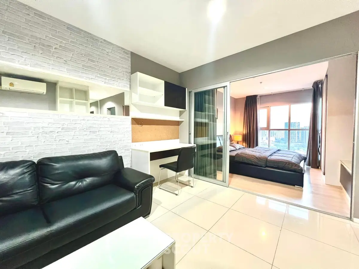 Modern apartment with open living room and bedroom, featuring sleek furniture and city view.