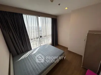Bright bedroom with large window and wooden flooring, offering a cozy and inviting atmosphere.