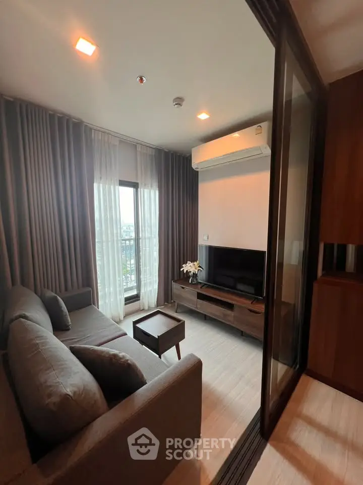 Modern living room with sleek furniture and large window offering natural light and city view.