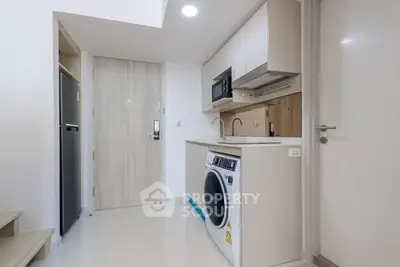 Modern compact kitchen with washing machine and microwave in sleek apartment.