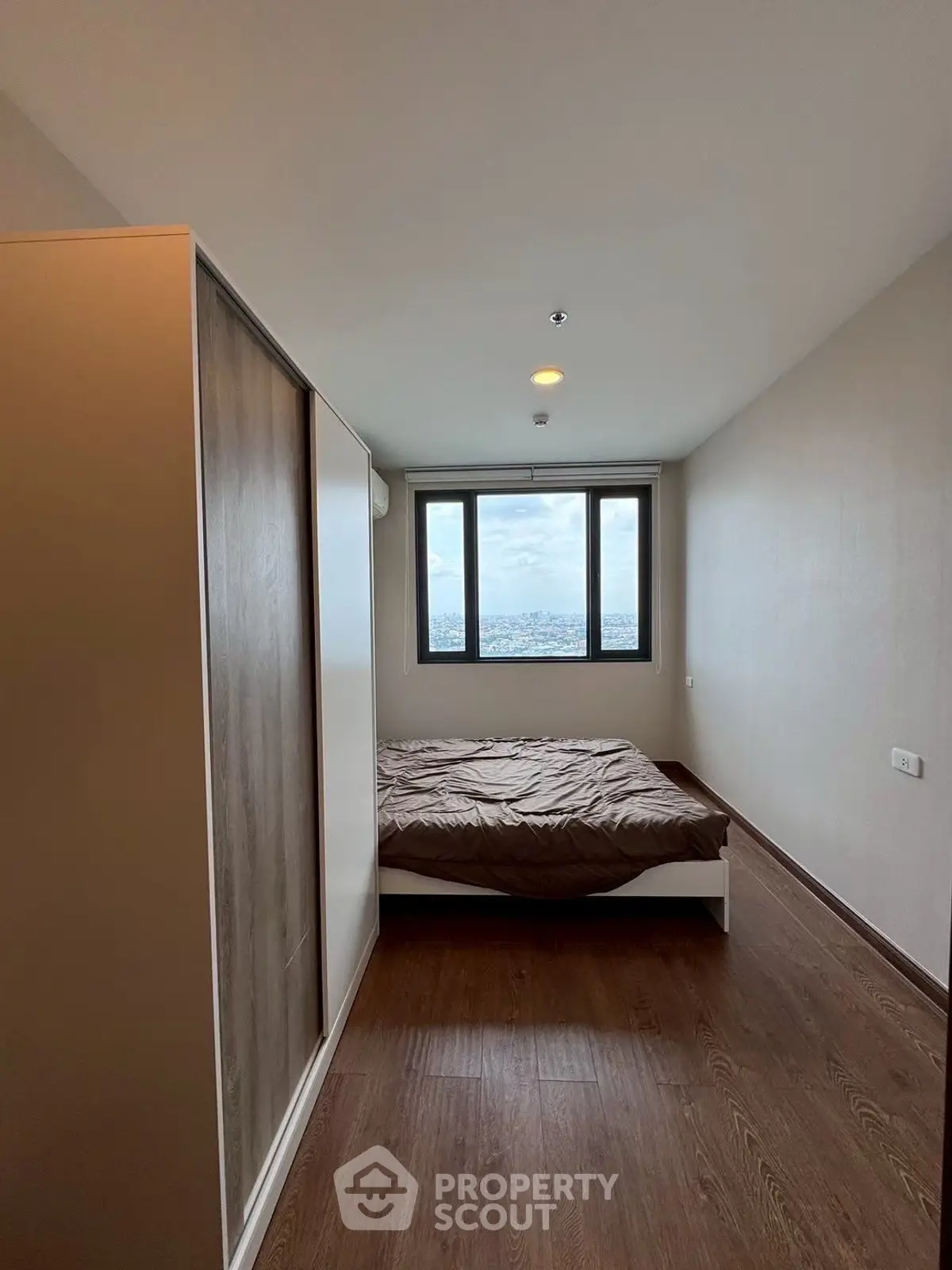 Modern bedroom with large window offering stunning city view, featuring sleek wooden flooring and minimalist design.