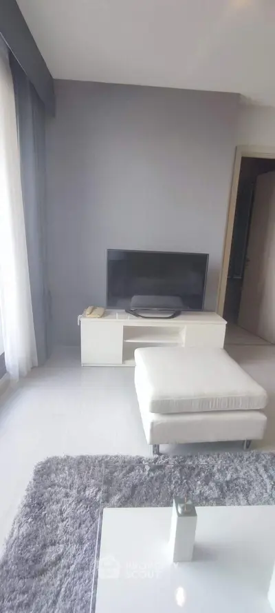 Modern living room with sleek TV stand and cozy ottoman in bright apartment.