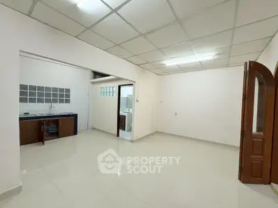 Spacious open-plan living area with tiled flooring and adjacent kitchen space.