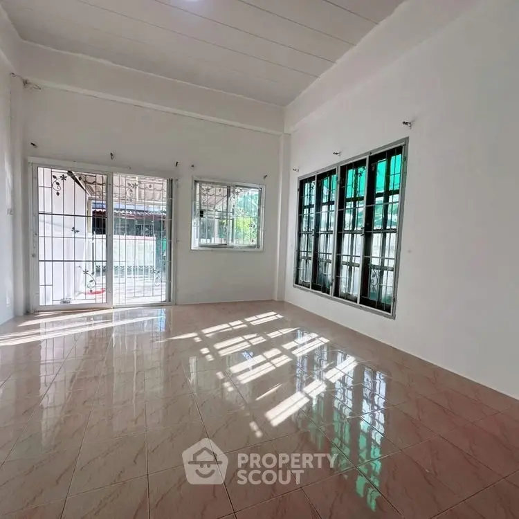 Spacious sunlit room with large windows and tiled flooring, perfect for versatile living space.