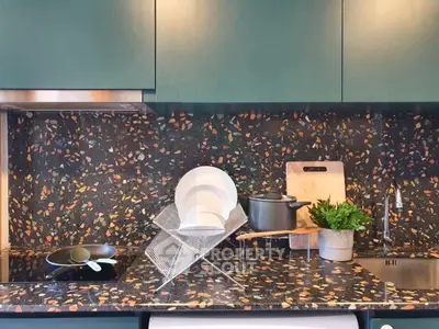 Modern kitchen with terrazzo backsplash and sleek cabinetry, featuring a dish rack and cooking essentials.