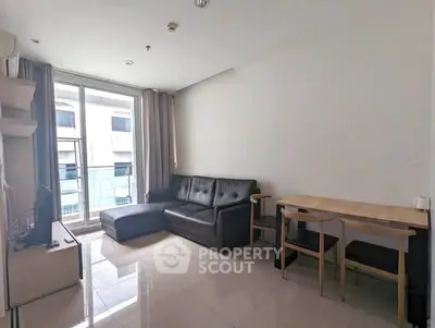 Modern living room with sleek black sofa and dining area, featuring large windows for natural light.
