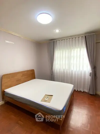 Spacious bedroom with large window and elegant curtains, featuring a comfortable bed and wooden flooring.