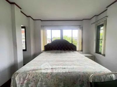 Cozy bedroom with large windows and floral bedspread, offering a serene view.