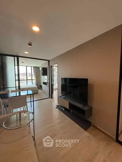 Modern living room with sleek TV setup and view into a cozy bedroom, featuring elegant wooden flooring.