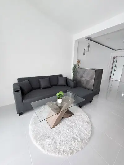 Modern living room with sleek gray sofa and stylish glass coffee table on plush white rug.