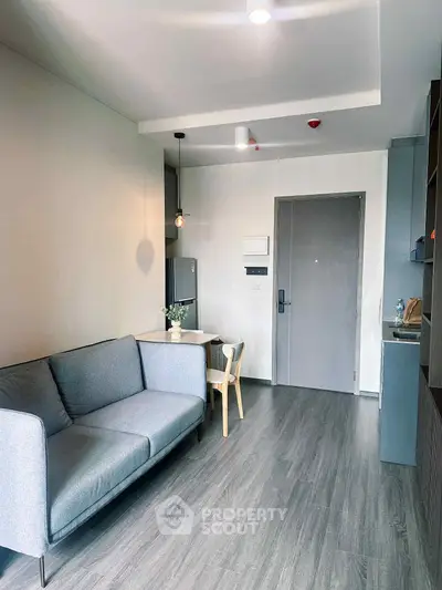 Modern living room with sleek grey sofa and stylish dining area in open layout apartment.