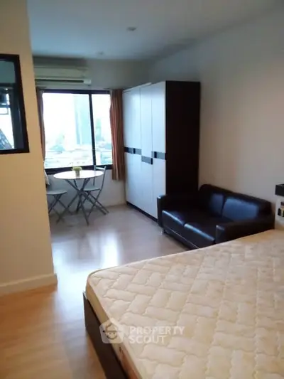 Cozy bedroom with large window, wardrobe, and small seating area in modern apartment.