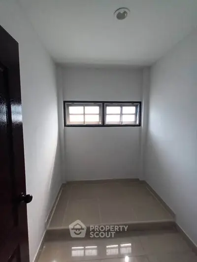 Compact storage room with tiled floor and small window, ideal for organizing essentials.