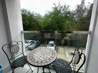 Charming balcony with stylish mosaic table and chairs overlooking lush greenery and parking area.