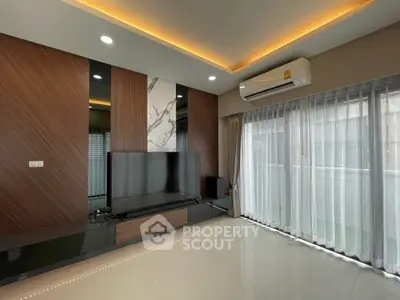 Modern living room with sleek design, large TV, and natural light from floor-to-ceiling windows.