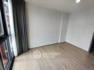 Spacious empty room with large window and wooden flooring, perfect for customization.