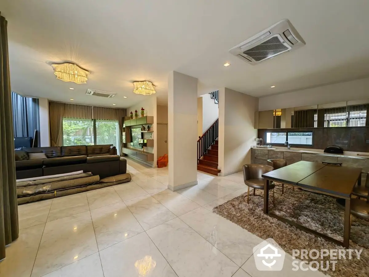 Spacious living room with gleaming tile floors, elegant chandeliers, plush seating, and an open layout leading to a modern kitchen.