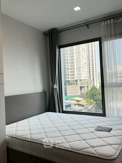 Modern bedroom with large window offering city view in high-rise apartment.